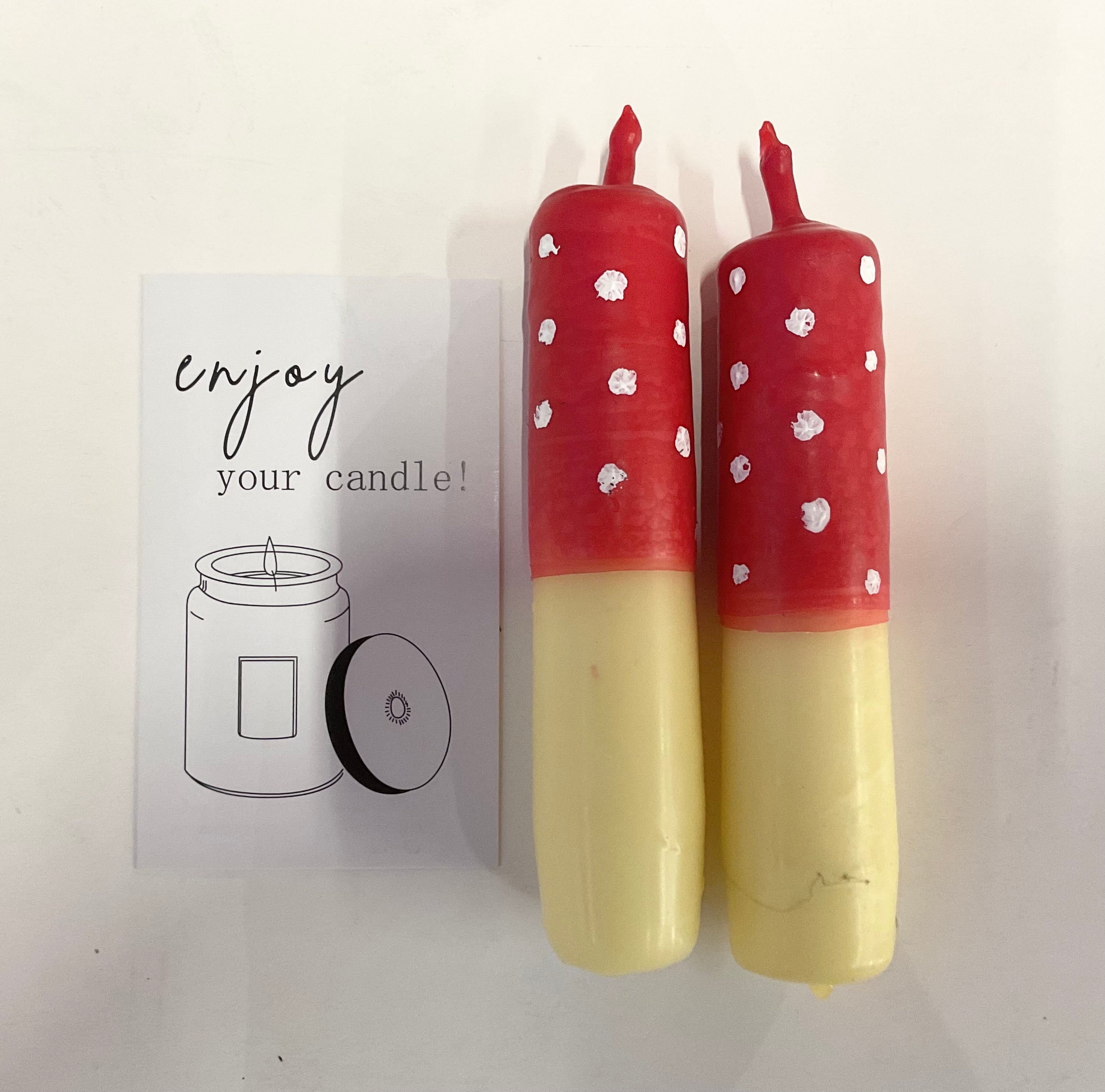 Two red and yellow candles with white polka dots on a white background, accompanied by a card with text and a candle illustration.