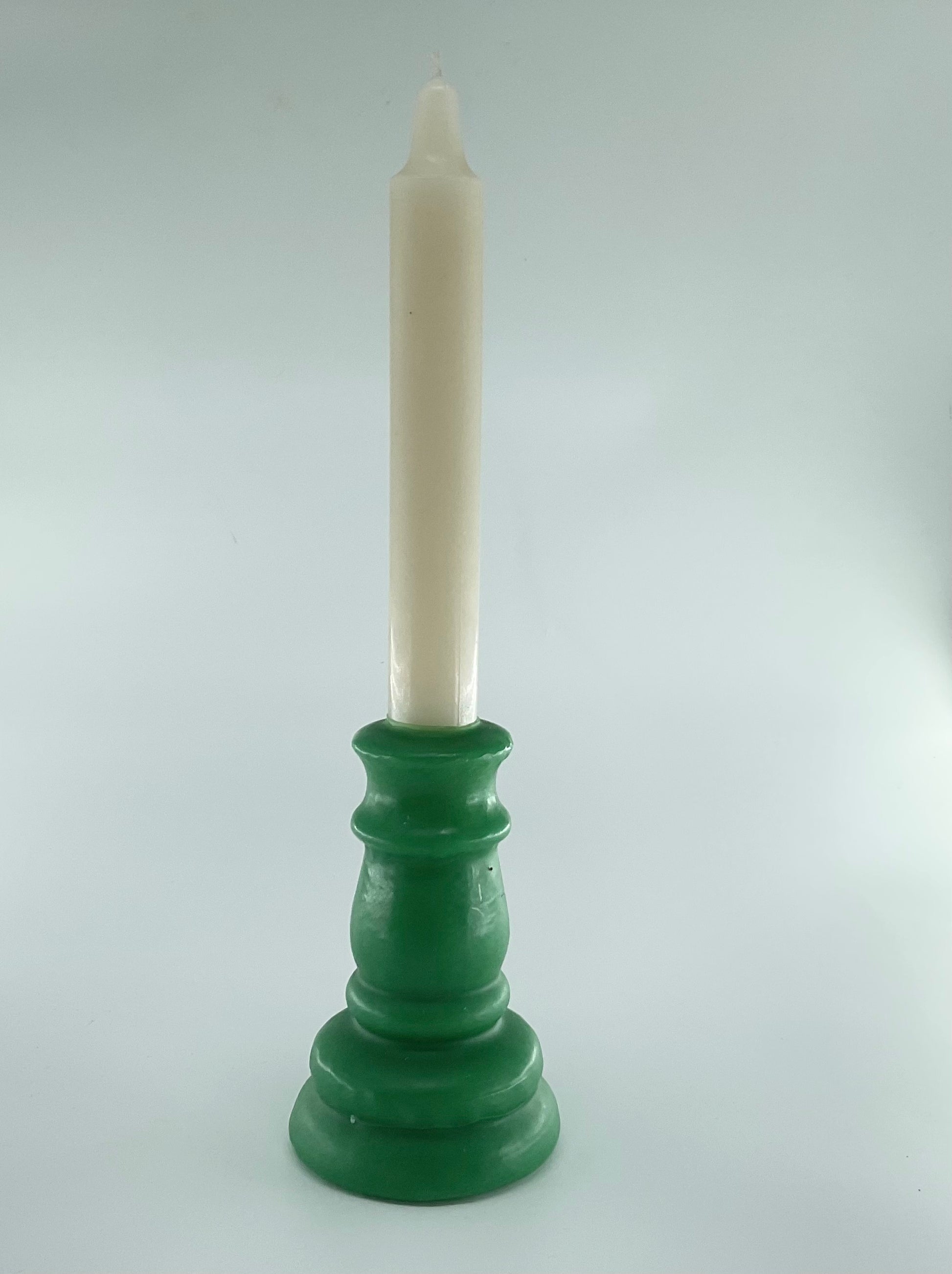 Green candle holder with a white candle on a light gray background