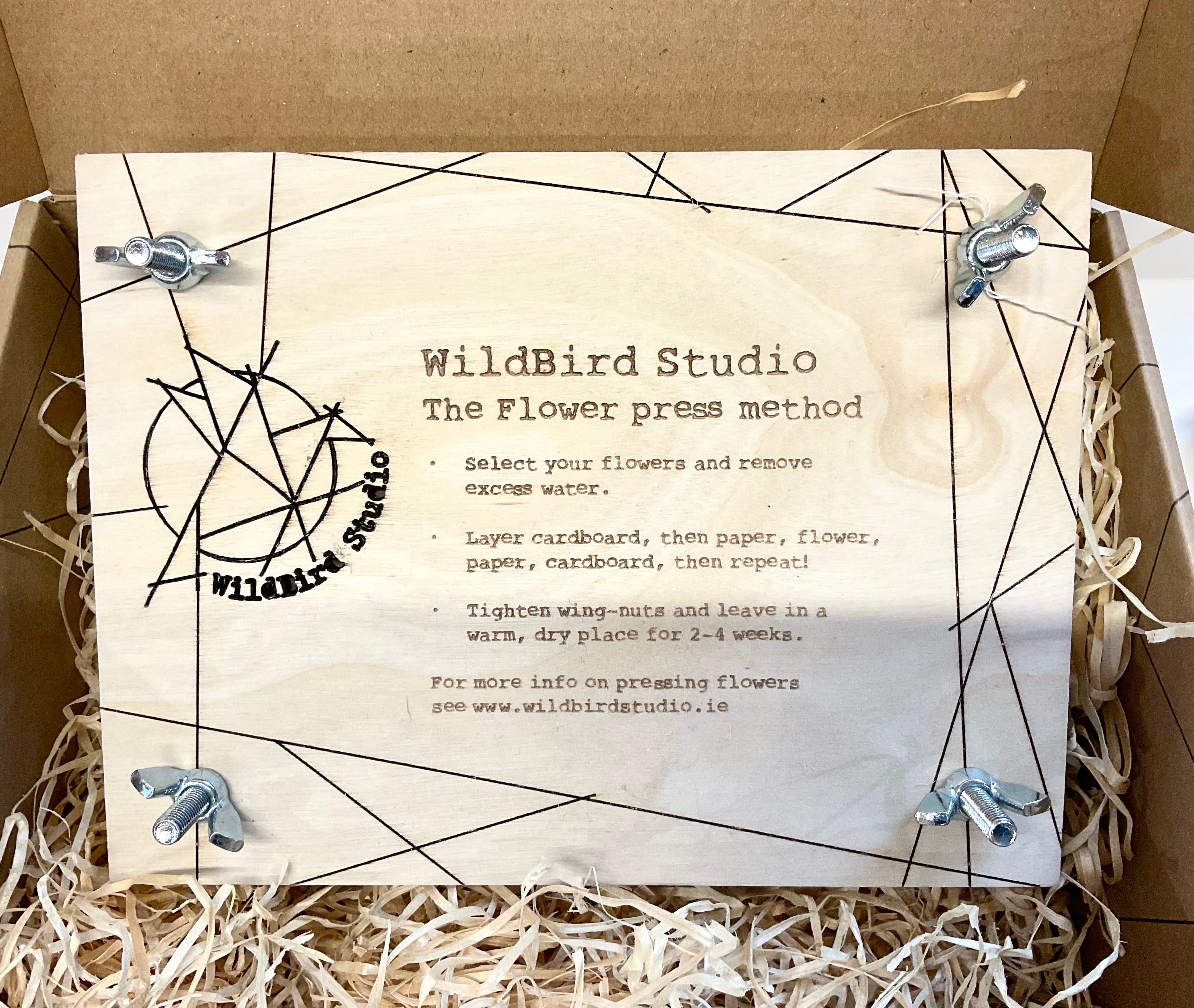 Flower press with WildBird Studio branding and instructions on a cardboard background