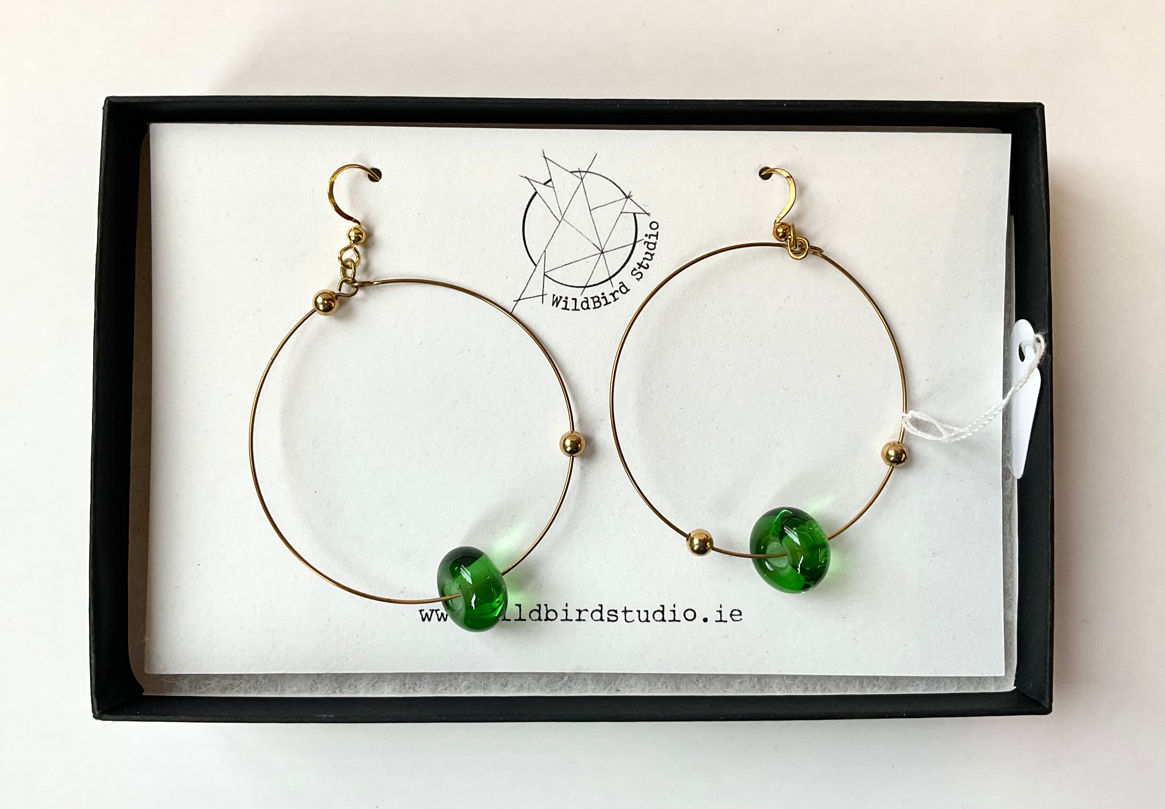 Gold hoop earrings with green beads on a branded card
