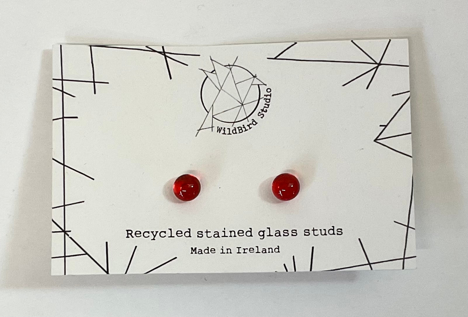 Red glass earrings on a card with 'wildBird studio' branding and text about recycled stained glass.