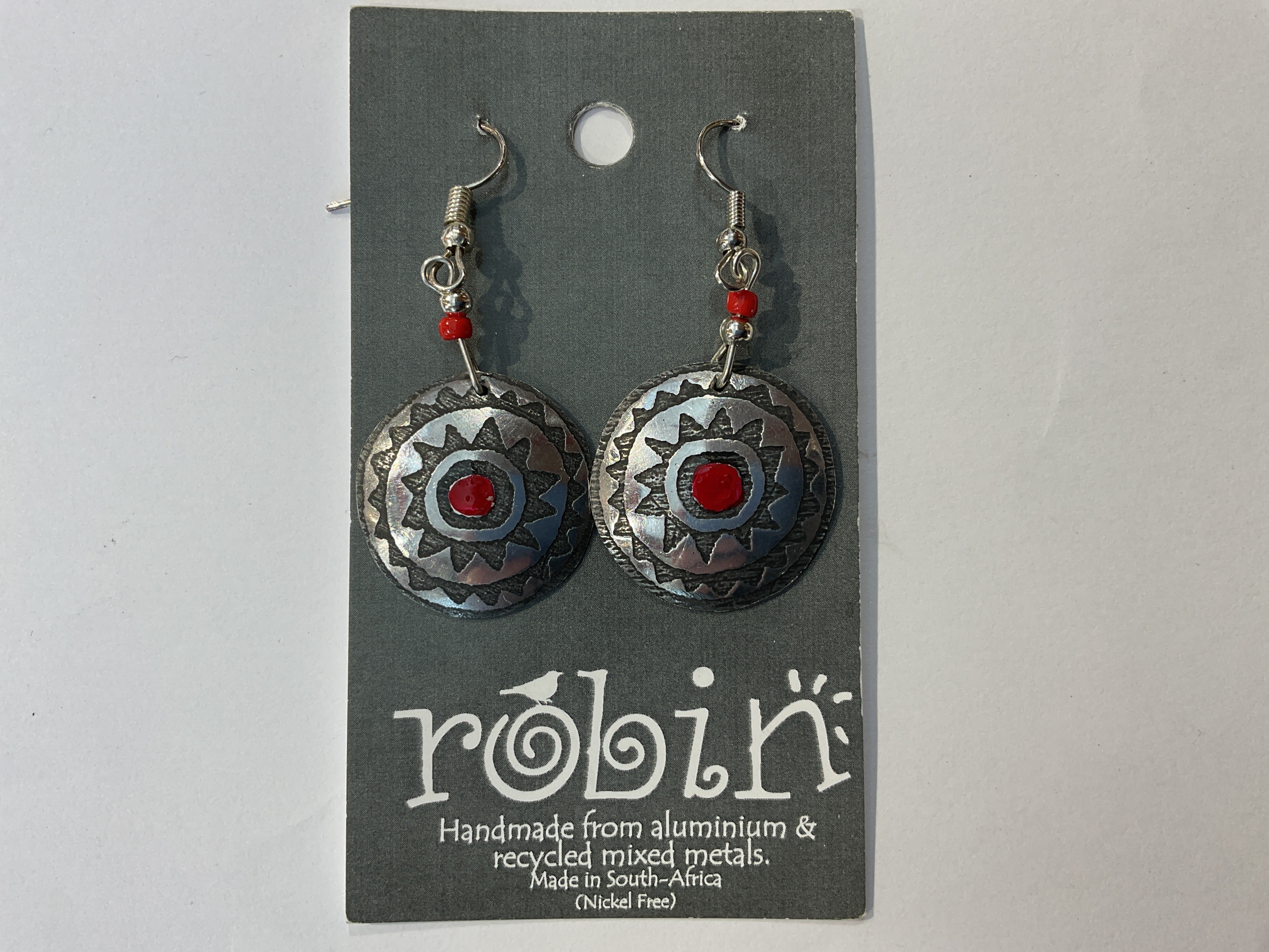 A pair of silver-colored earrings with red and black patterns, made from recycled metals, displayed on a card with 'Robin' branding.
