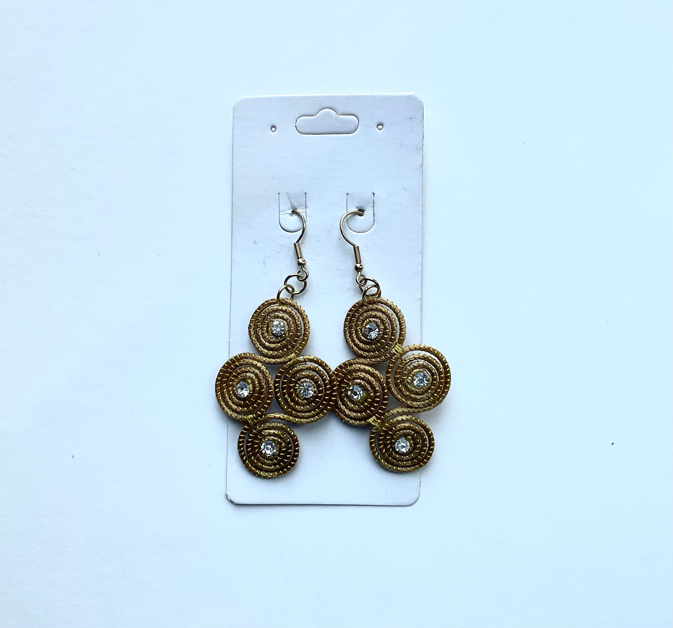 Pair of gold grass earrings on a white card against a light white background