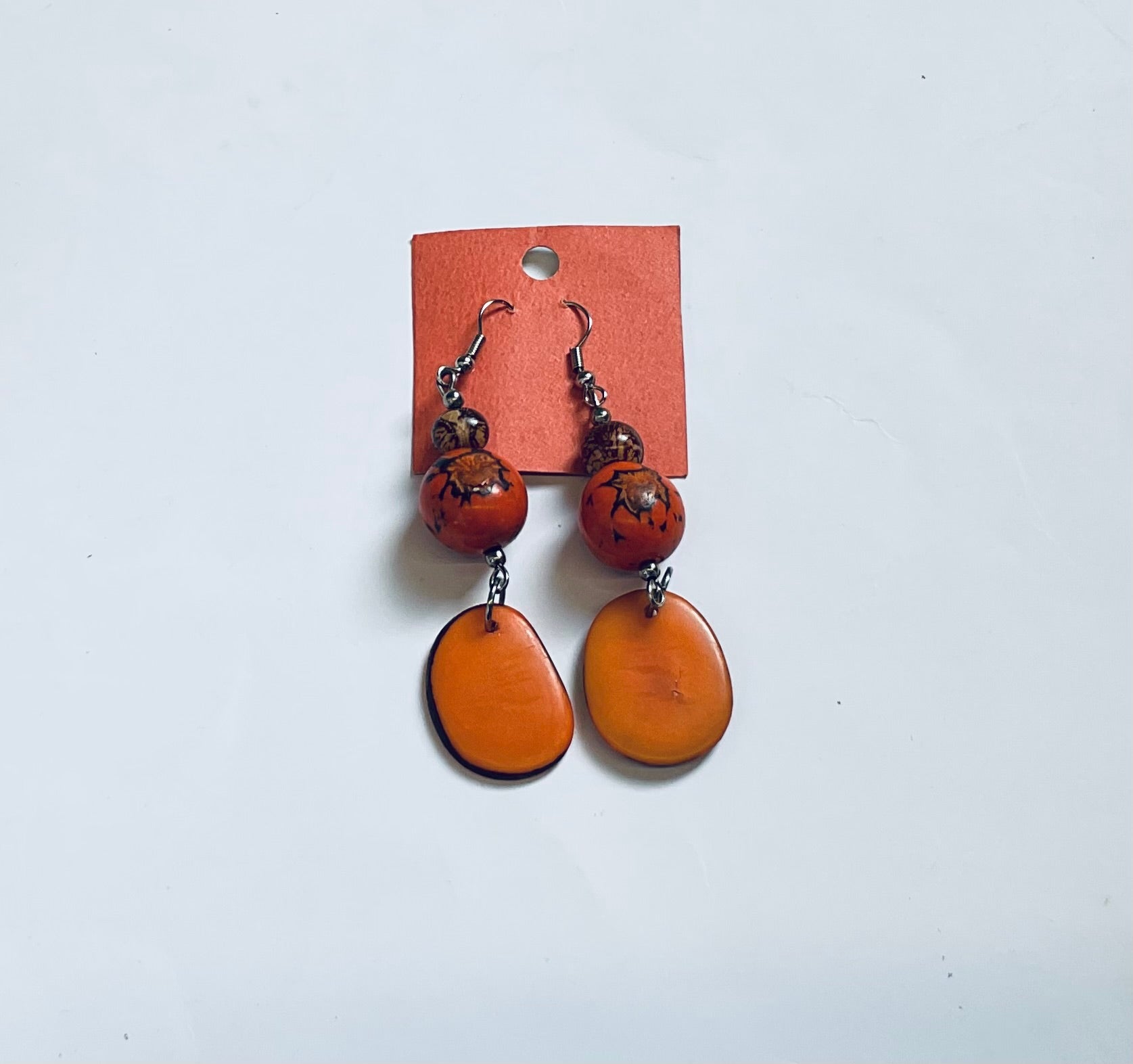 Pair of orange earrings on a white background with a brown card.