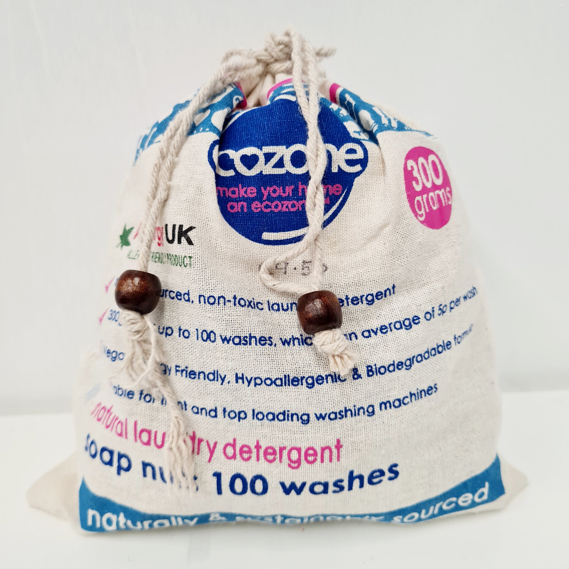 A beige drawstring bag labeled 'Ecozone' with a blue label that reads '300g', '100 washes', and 'Natural & Friendly'. There are also text highlights about the product being a top-loading washing machine, not being a skin irritant, and being sourced from recyclable materials.