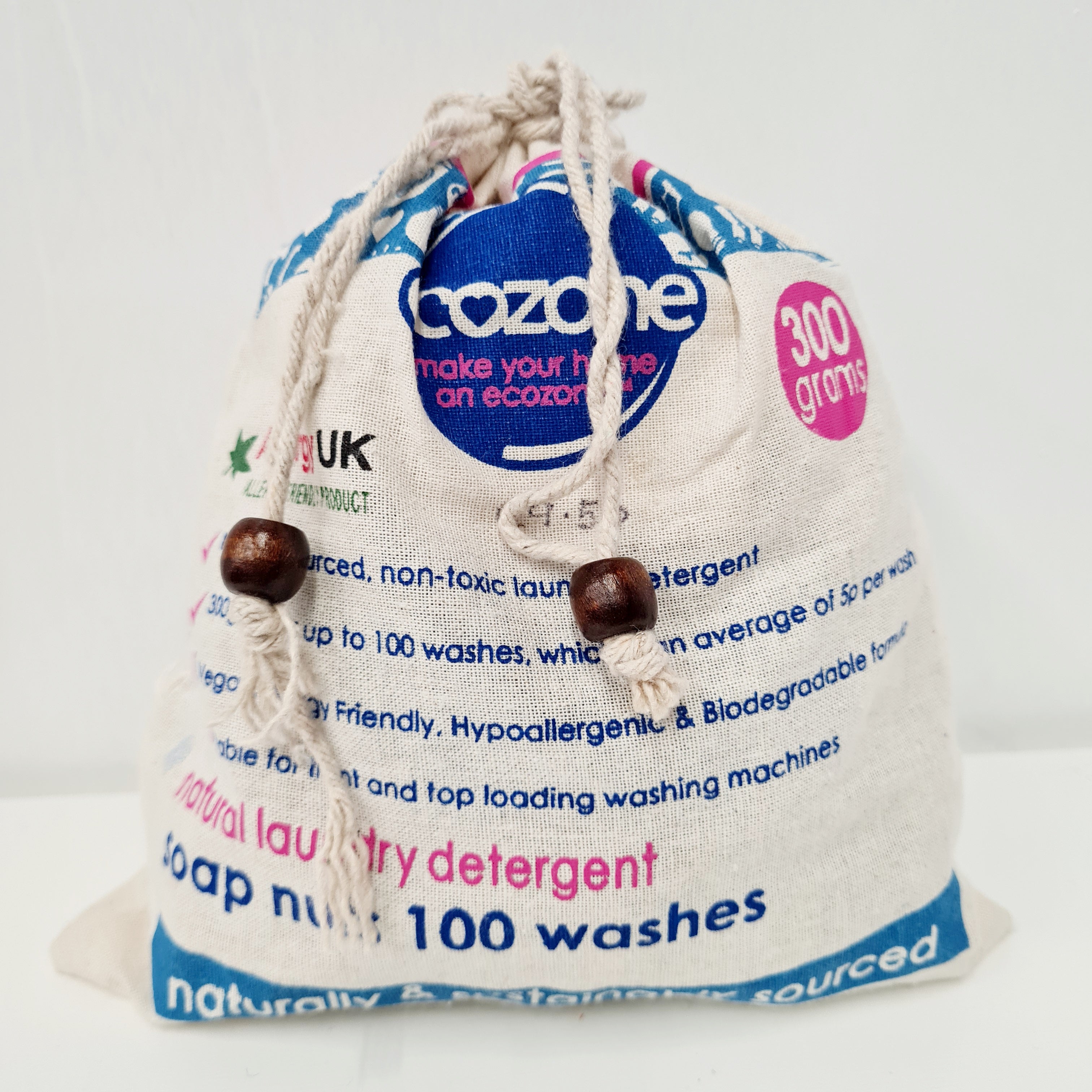 A beige drawstring bag labeled 'Ecozone' with a blue label that reads '300g', '100 washes', and 'Natural & Friendly'. There are also text highlights about the product being a top-loading washing machine, not being a skin irritant, and being sourced from recyclable materials.