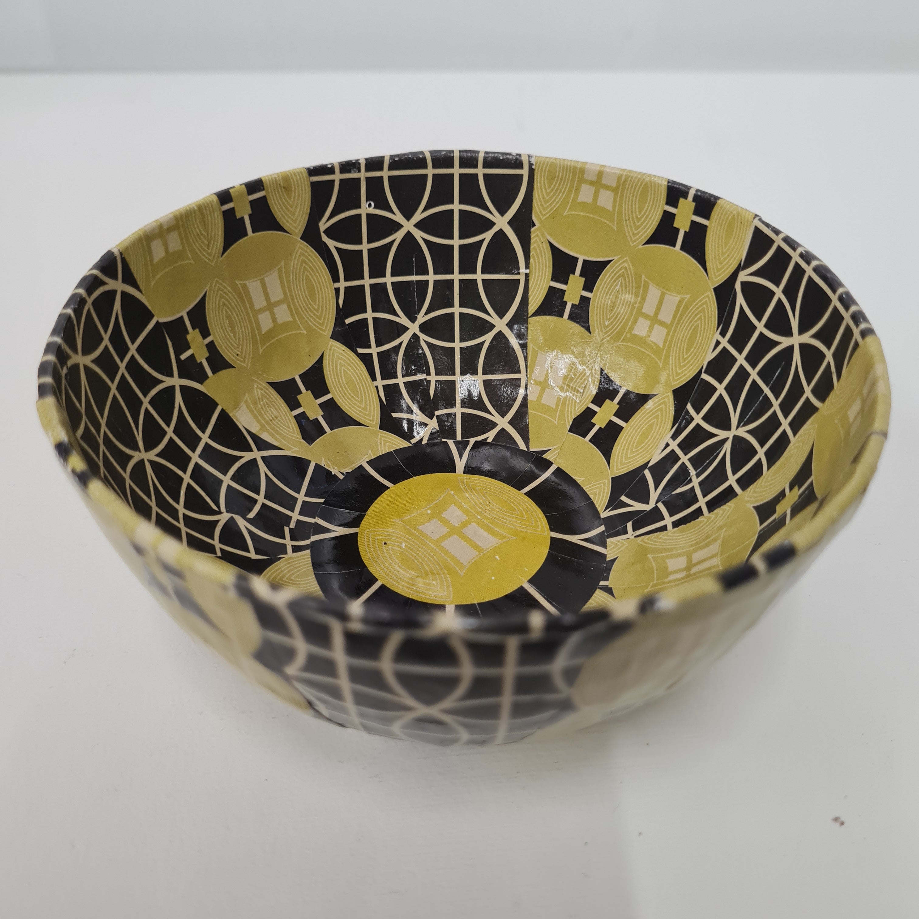 A round paper mache bowl with a yellow and black geometric pattern.