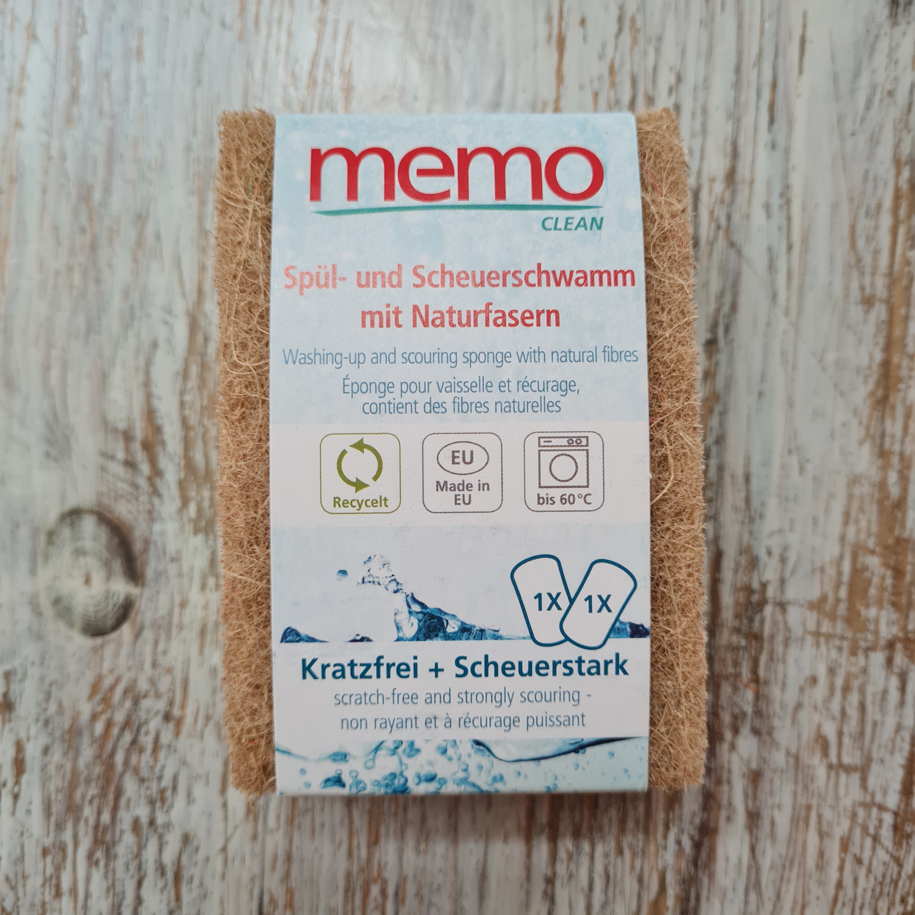 A Memo brand cleaning sponge in natural color, packaged in a cardboard box with blue and white design, highlighting its natural fibers and suitability for dishwashing and scouring.
