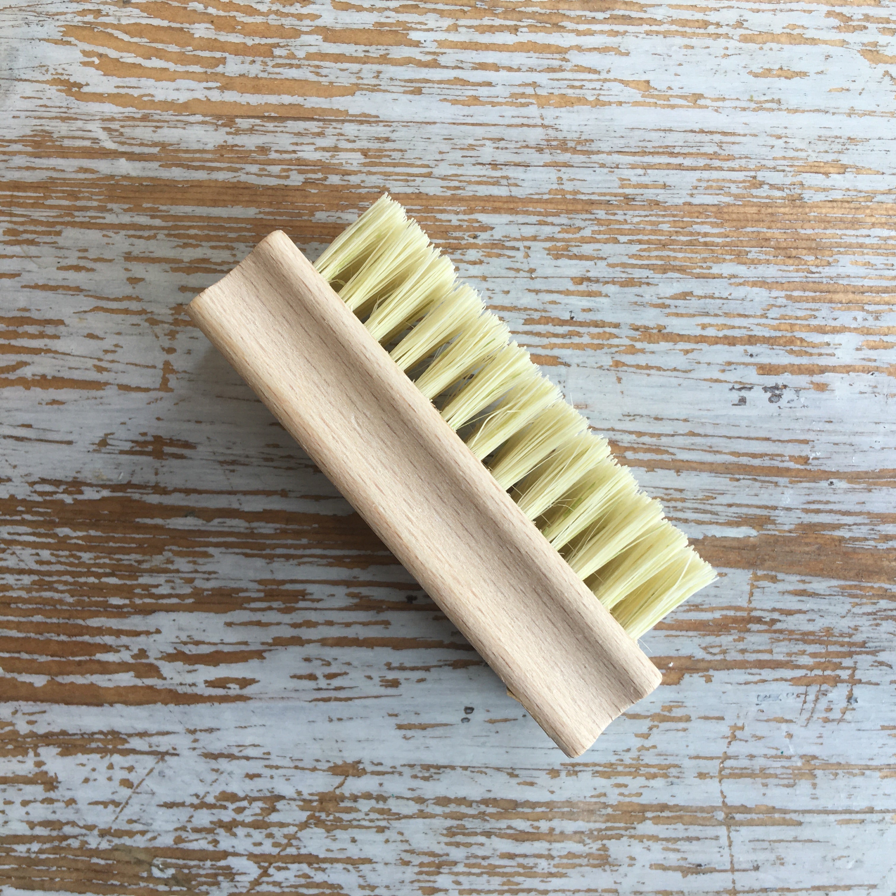 A wooden nail brush with natural bristles lying on a wooden surface.