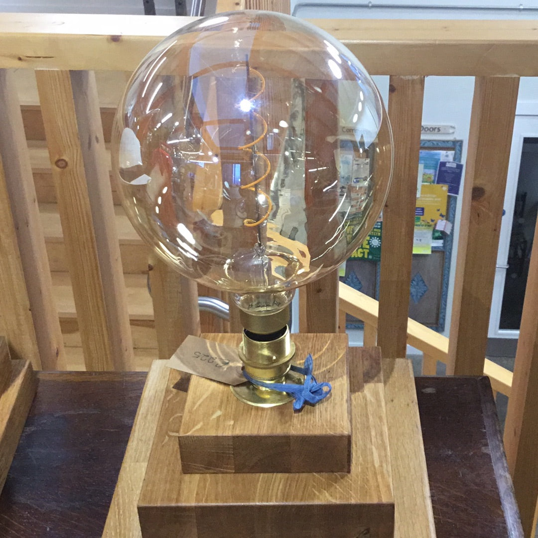 A square-shaped lamp with a glass bulb and a brass base, upcycled by Steampunk, displayed on a wooden surface.