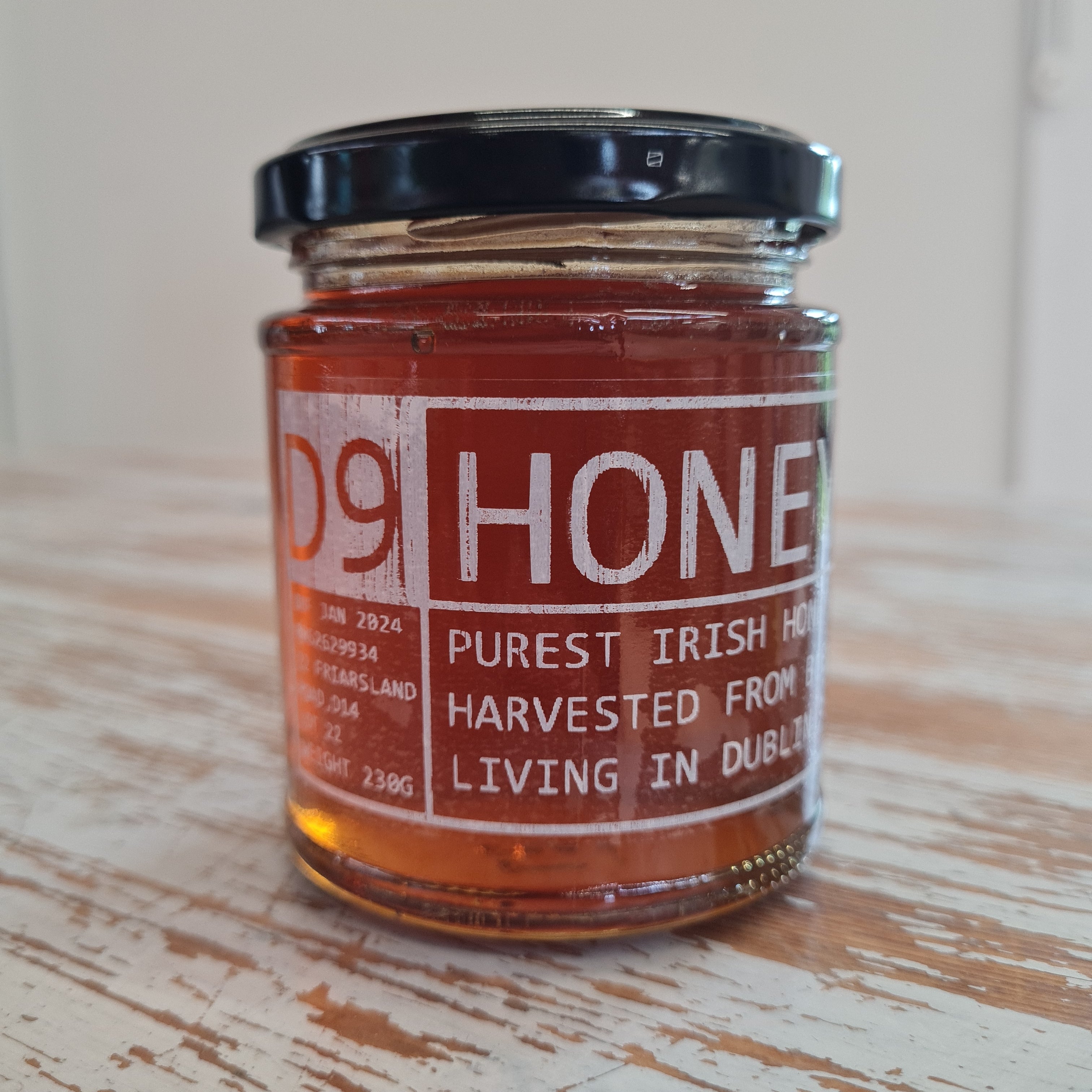 A jar of Dublin 9 Honey placed on a wooden surface, with a label that reads 'D9 HONEY - PUREST IRISH HONEY HARVESTED FROM LIVING IN DUBLIN'.