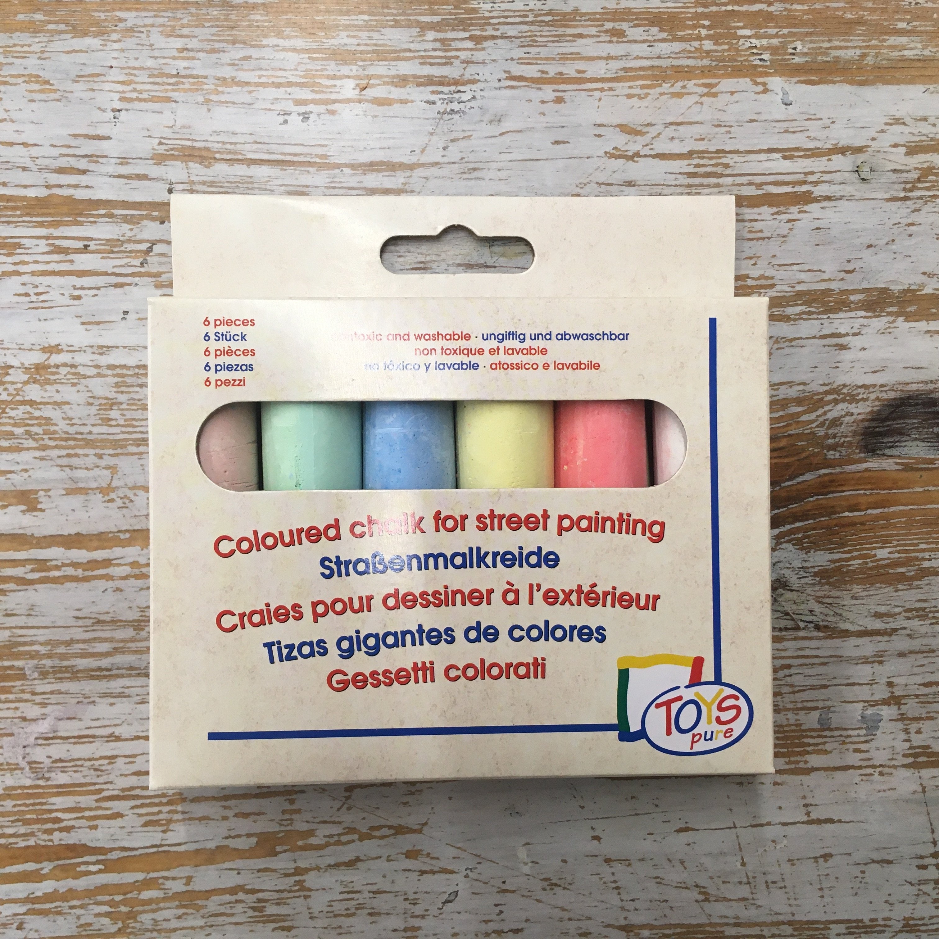 A pack of multi-colored chalk for street painting displayed on a wooden surface.